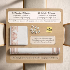 May include: A rolled-up and folded white and pink desk mat with a lotus flower design, along with a set of mahjong tiles, and a DESKNEKO sticker, are displayed on a wooden surface. The image also includes text about shipping options.