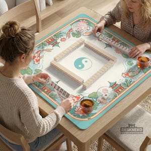 May include: A wooden mahjong table with a decorative mat featuring koi fish, pagodas, and a yin-yang symbol. The table is set for a game, with tiles arranged in a square and players holding racks of tiles. The mat has a teal border.