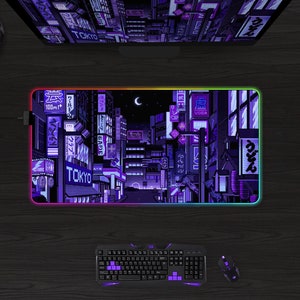 May include: A rectangular gaming mouse pad with a pixelated cityscape design in shades of purple and black, with the word "TOKYO" visible. The pad has a glowing, multi-colored edge. A keyboard, mouse, and headphones are also visible.