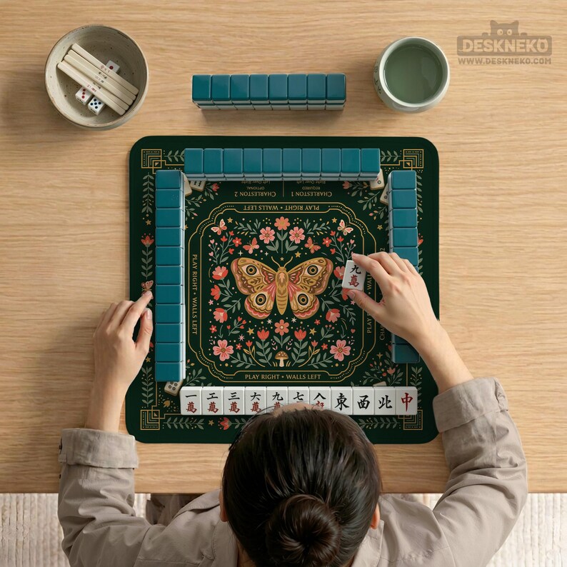 May include: A square mahjong mat featuring a dark green background with a central butterfly illustration surrounded by floral motifs. The mat includes text labels for gameplay, with rows of teal tiles arranged around the perimeter.