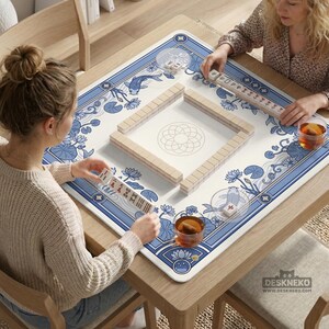 May include: A square Mahjong game table with a blue and white floral design. The table is set for a game, with tiles arranged in a square and players holding tiles. The table has a wooden frame and is set on a wooden table.