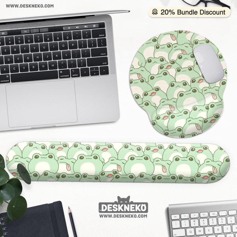 May include: A computer desk setup featuring a laptop, mouse, and keyboard. The set includes a green frog-themed mousepad, wrist rest, and a white mouse. The frog design is repeated across the accessories. The website address is visible.