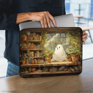 Può includere: Custodia per laptop con un'illustrazione di un fantasma in una biblioteca. Il design include scaffali, piante in vaso e una finestra, creando una scena affascinante. La custodia è nera con il testo "DESKNEKO" in basso.