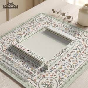 May include: A Mahjong set with ivory tiles on a floral mat. The mat has a light green border and a cream centre. A small white vase is in the background. The set is ready for play.