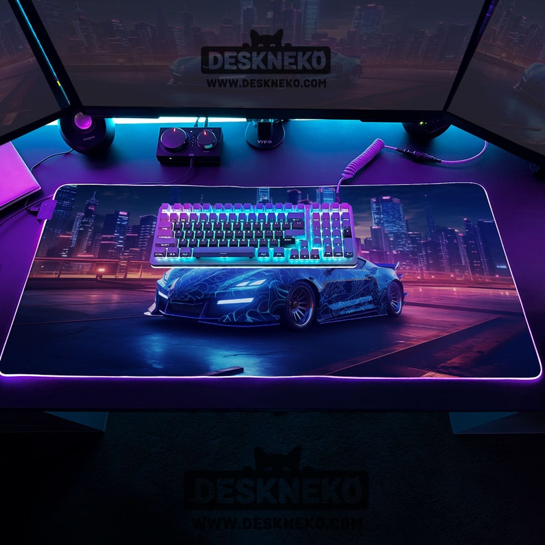May include: A rectangular gaming mouse pad with a car graphic and a keyboard. The pad has a neon edge and the text "DESKNEKO" and "www.deskneko.com". The keyboard has blue and purple lights.