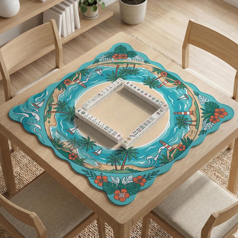May include: A square wooden table with a decorative mat featuring a tropical island scene. The mat has a turquoise border with palm trees, sailboats, and a lighthouse. A Mahjong set is placed on the mat.