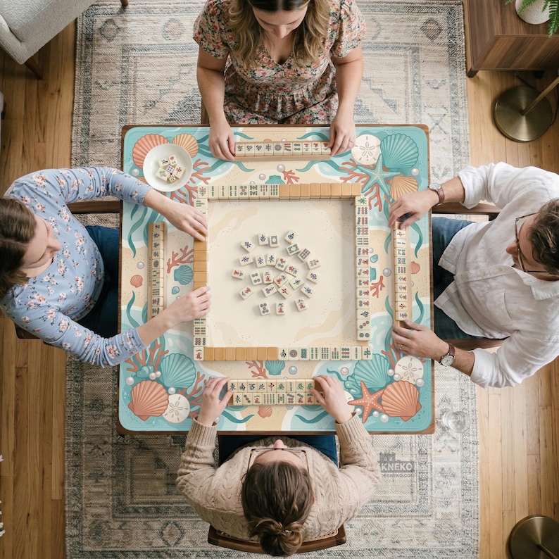 May include: A square mahjong table featuring a light blue surface with a colorful seashell and coral pattern. Four players are seated around the table, which is set with ivory-colored mahjong tiles arranged in rows and a central pile.