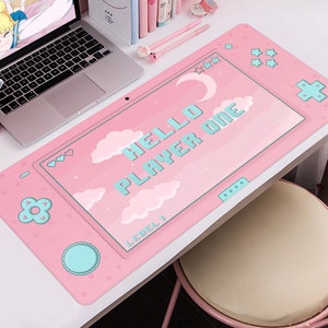 K&ouml;nnte beinhalten: Rosa Schreibtischunterlage mit einem Videospiel-Controller-Design. Die Matte zeigt den Text "HELLO PLAYER ONE" in pixeligen blauen Buchstaben sowie Wolken, Herzen und Sterne. Ein Laptop, Stifte und eine Maus sind ebenfalls zu sehen.