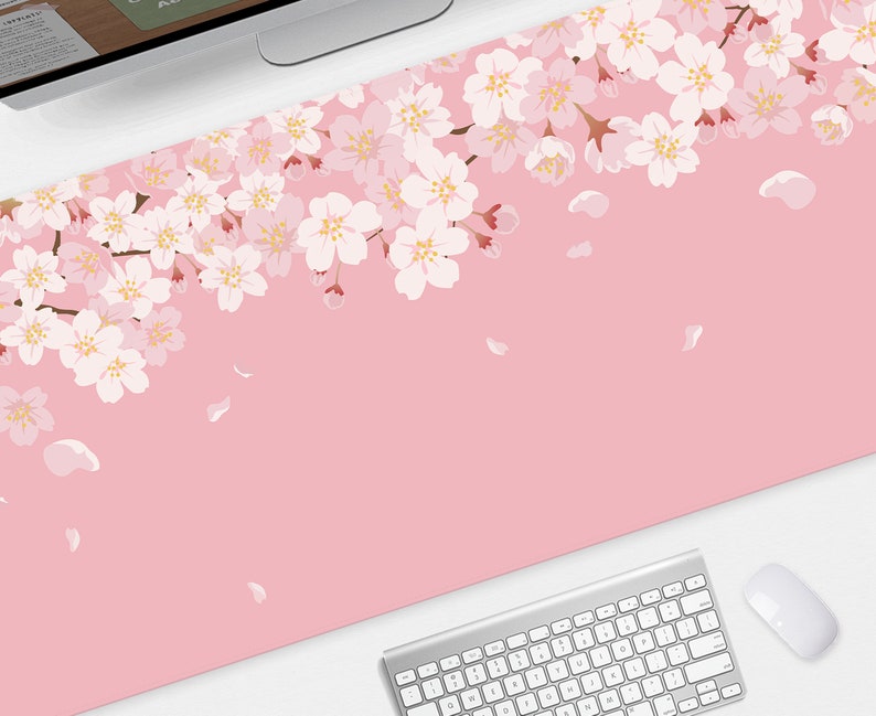 May include: A pink desk mat featuring a floral cherry blossom design. The blossoms are white and pink, with falling petals. A computer keyboard and mouse are visible at the bottom of the mat.