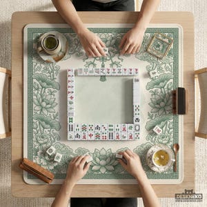 Puede incluir: Vista cenital de un juego de Mahjong en curso. El juego est&aacute; sobre una alfombra beige claro con un borde floral verde y dise&ntilde;os de flores de loto. Se ven las manos de los jugadores, colocando las fichas. Tazas de t&eacute; y accesorios tambi&eacute;n est&aacute;n sobre la mesa.