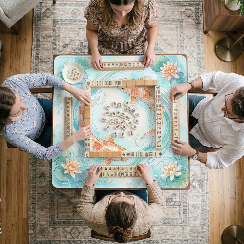 May include: A square mahjong table featuring a light blue surface with a printed koi fish and lotus flower design. The table is set with a central pile of white mahjong tiles and four racks containing rows of tiles, arranged for a four-player game.