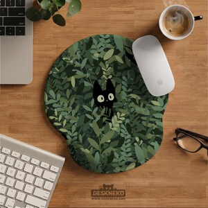 May include: A circular mouse mat with a design of a black cat amongst green leaves. The mouse mat has a wrist rest. The text "DESKNEKO" is at the bottom. A white mouse, keyboard, and coffee cup are also visible.