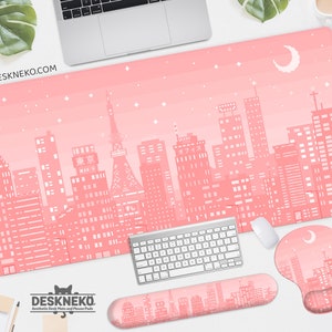 May include: Aesthetic desk setup featuring a pink desk mat with a pixelated cityscape design, a keyboard, mouse, and wrist rest. The mat has a Tokyo-inspired skyline with a crescent moon and stars. The website address is visible on the mat.