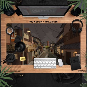 Op de afbeelding: Een rechthoekige bureaumat met een illustratie van een Japanse straatscène. De mat meet 100 x 60 cm en toont een gedetailleerde tekening van gebouwen, een pagode en een weg. Een toetsenbord, muis en andere bureau-accessoires zijn rond de mat gerangschikt.