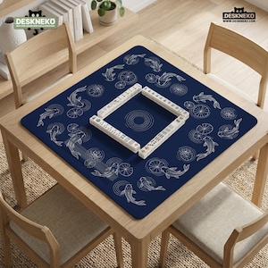 Puede incluir: Un tapete de mahjong azul marino con un dise&ntilde;o de peces koi y nen&uacute;fares. El tapete est&aacute; sobre una mesa de madera con cuatro sillas. Las fichas de mahjong est&aacute;n dispuestas en un cuadrado en el centro. La marca "DESKNEKO" es visible.