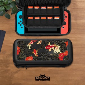 以下が含まれることがあります： 黒色のキャリングケース。 鯉のデザイン、赤と金のアクセント、そして「DESKNEKO」の文字が特徴です。 ケースは開いており、青と赤のゲーム機とゲームカートリッジの収納スペースが見えます。