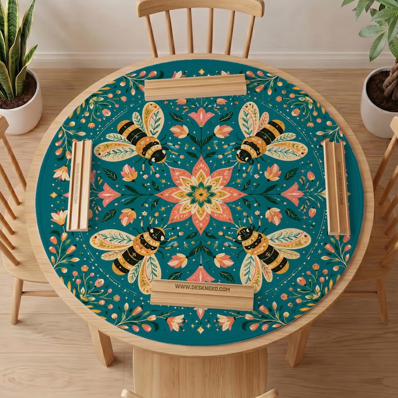 May include: A round teal table mat featuring a symmetrical pattern of four bees and a central floral motif in shades of pink, yellow, and green. The mat is accented with four light wood rectangular holders, each printed with the text WWW.DESKNEKO.COM.