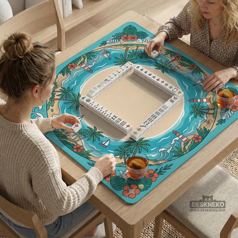 May include: A wooden table with a turquoise mat depicting a tropical beach scene, framing a Mahjong set with white tiles. Two people are playing Mahjong, with cups of tea on the table. The table has the text "DESKNEKO" on the bottom right.