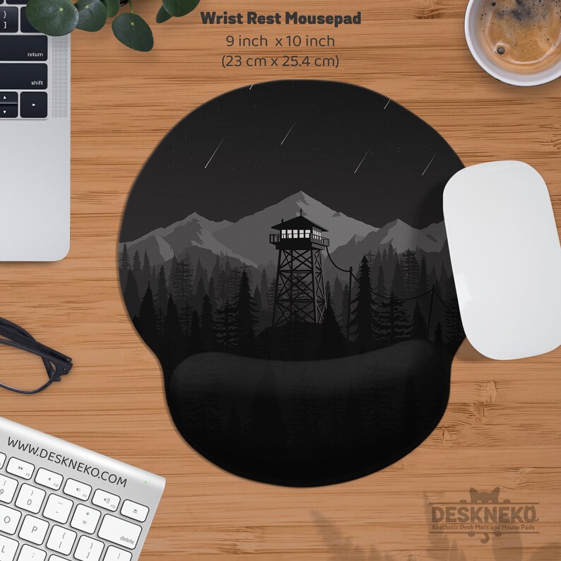 May include: Black and gray wrist rest mousepad with a forest and mountain scene. The mousepad is 9 inches by 10 inches. The design features a watchtower, trees, and mountains under a starry sky. A white mouse and keyboard are also visible.