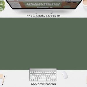 May include: A large, olive green desk mat, measuring 47 x 23.5 inches, dominates the image. A white keyboard, mouse, and notepad are positioned below. The website address, www.deskneko.com, is visible at the bottom.