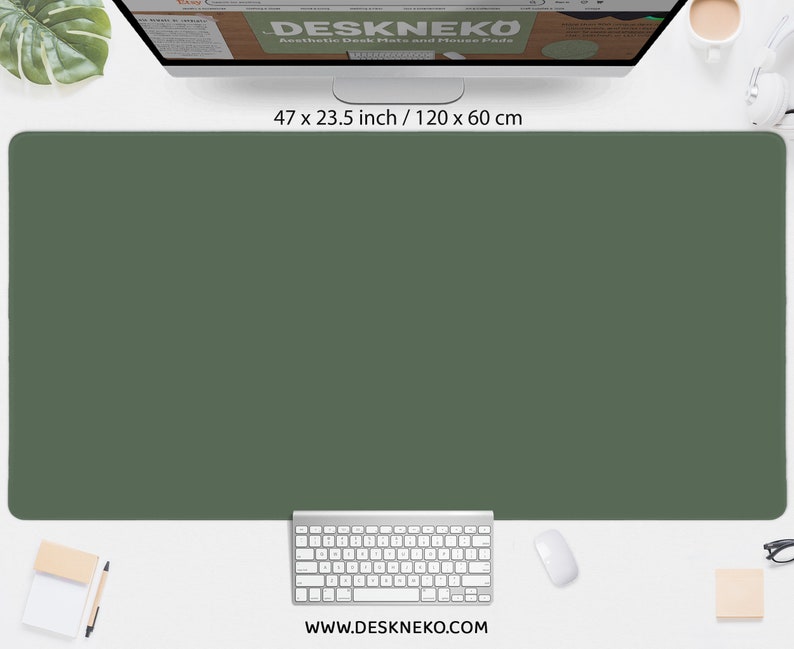 May include: A large, olive green desk mat, measuring 47 x 23.5 inches, dominates the image. A white keyboard, mouse, and notepad are positioned below. The website address, www.deskneko.com, is visible at the bottom.