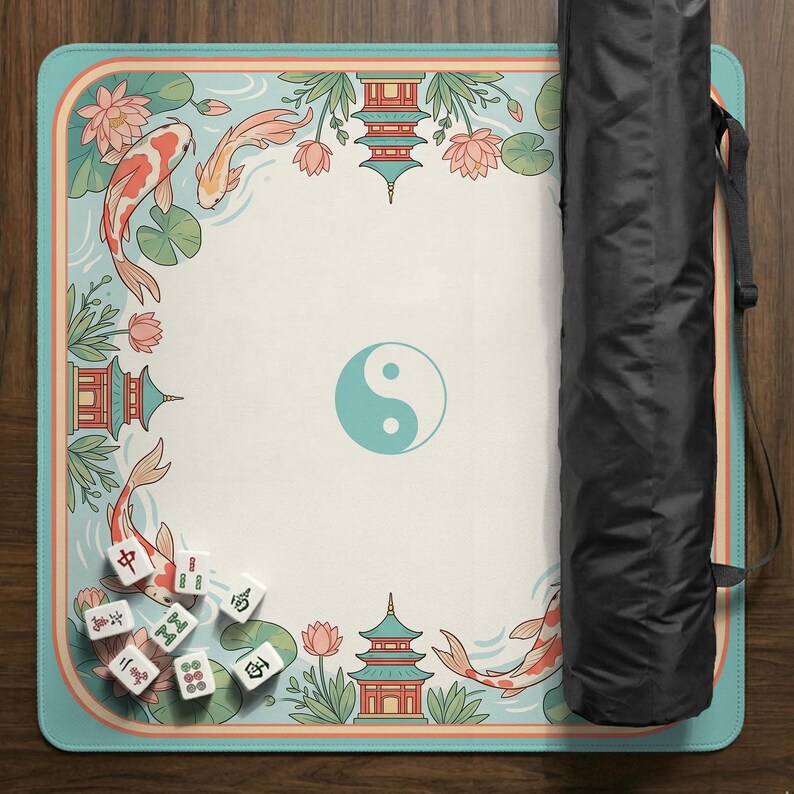 May include: A Mahjong game mat with a teal border and a cream-colored center. The mat features koi fish, lotus flowers, pagodas, and a teal yin-yang symbol. A black carrying case is visible on the right side, and several Mahjong tiles are scattered on the mat.