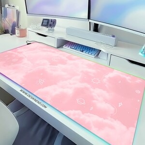 May include: A rectangular pink mouse pad with a cloud design and white celestial illustrations. The mouse pad has a colorful LED edge and the website address www.deskneko.com printed on the bottom left corner.