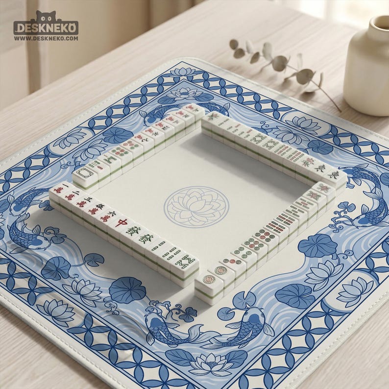 May include: A Mahjong set with white tiles and red and green markings is arranged on a blue and white patterned mat. The mat features koi fish and lotus flower designs. The logo "DESKNEKO" is visible in the top left corner.
