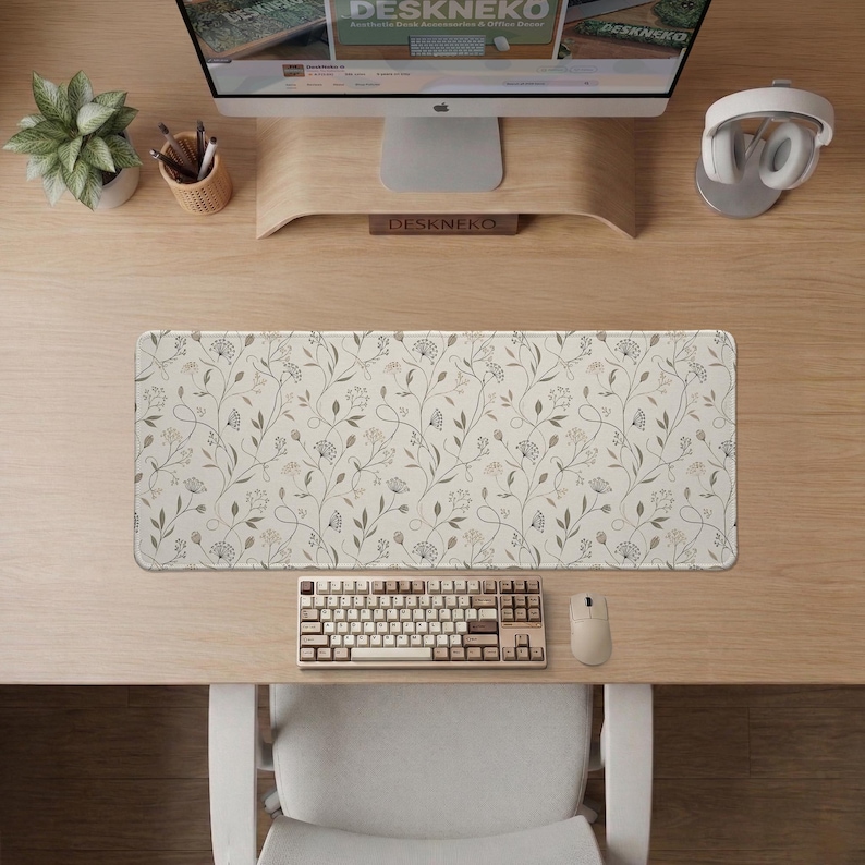 Pu&ograve; includere: Un tappetino da scrivania rettangolare con un motivo botanico ripetuto di delicate viti, foglie e piccoli fiori grigi e beige su uno sfondo color crema. Il tappetino &egrave; posizionato su una scrivania in legno sotto un monitor e una tastiera.