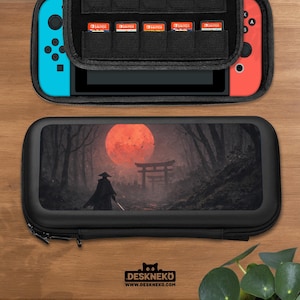 Może przedstawiać: Czarny futerał do przenoszenia Nintendo Switch z zamkiem błyskawicznym, z grafiką samuraja w lesie pod czerwonym księżycem. Etui jest otwarte, ukazując konsolę Switch i kartridże do gier. Widoczny jest tekst "DESKNEKO".