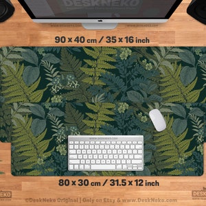 Pu&ograve; includere: Un tappetino da scrivania rettangolare con un motivo botanico di felci e foglie in tonalit&agrave; verdi e verde acqua. Il tappetino misura 90 x 40 cm e 80 x 30 cm. Una tastiera e un mouse sono posizionati sul tappetino. Il testo "DeskNeko" e gli indirizzi web sono visibili.
