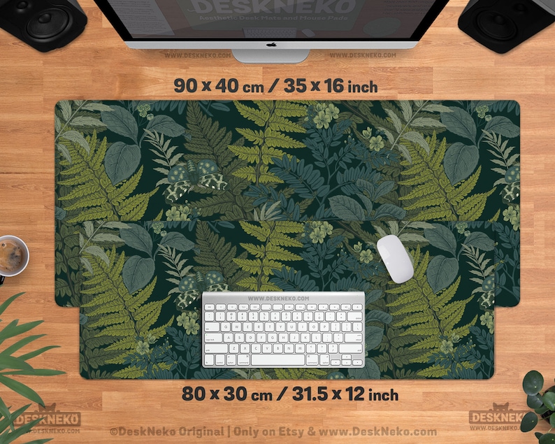 Pu&ograve; includere: Un tappetino da scrivania rettangolare con un motivo botanico di felci e foglie in tonalit&agrave; verdi e verde acqua. Il tappetino misura 90 x 40 cm e 80 x 30 cm. Una tastiera e un mouse sono posizionati sul tappetino. Il testo "DeskNeko" e gli indirizzi web sono visibili.