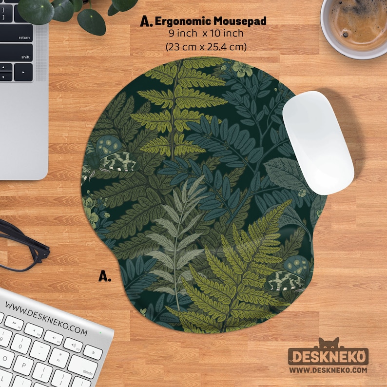 Pu&ograve; includere: Tappetino per mouse ergonomico con un design botanico di felci nei toni del verde e del blu. Il tappetino misura 23 cm x 25,4 cm e ha un poggiapolsi. Un mouse bianco &egrave; posizionato sul tappetino, con una tastiera e una tazza di caff&egrave; sullo sfondo.