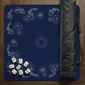 Puede incluir: Un tapete de Mahjong azul marino con un dise&ntilde;o de peces koi y nen&uacute;fares. El tapete incluye un juego de fichas de Mahjong y una funda de transporte negra. El tapete est&aacute; enrollado y listo para jugar.