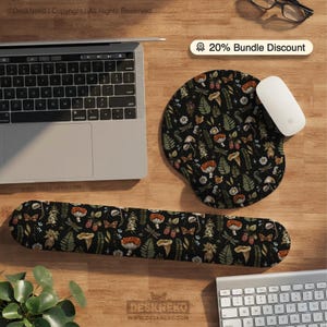 Peut inclure: Un ensemble de tapis de souris et de repose-poignets ergonomiques noirs avec un motif botanique de champignons, de papillons et de feuilles. Une souris blanche et un ordinateur portable sont également visibles. L'ensemble est conçu pour le confort et le style.