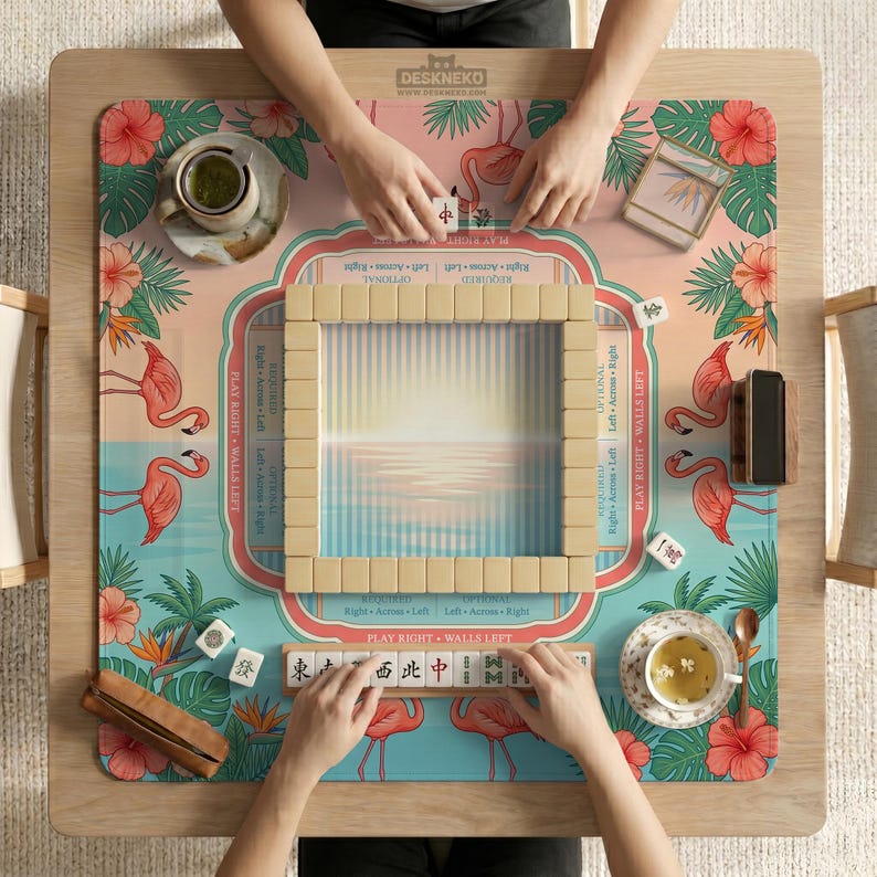 May include: A square mahjong game mat featuring a tropical design with pink flamingos, green palm leaves, and red hibiscus flowers. The mat has a central sunset gradient, game instructions, and a wooden rack holding mahjong tiles.
