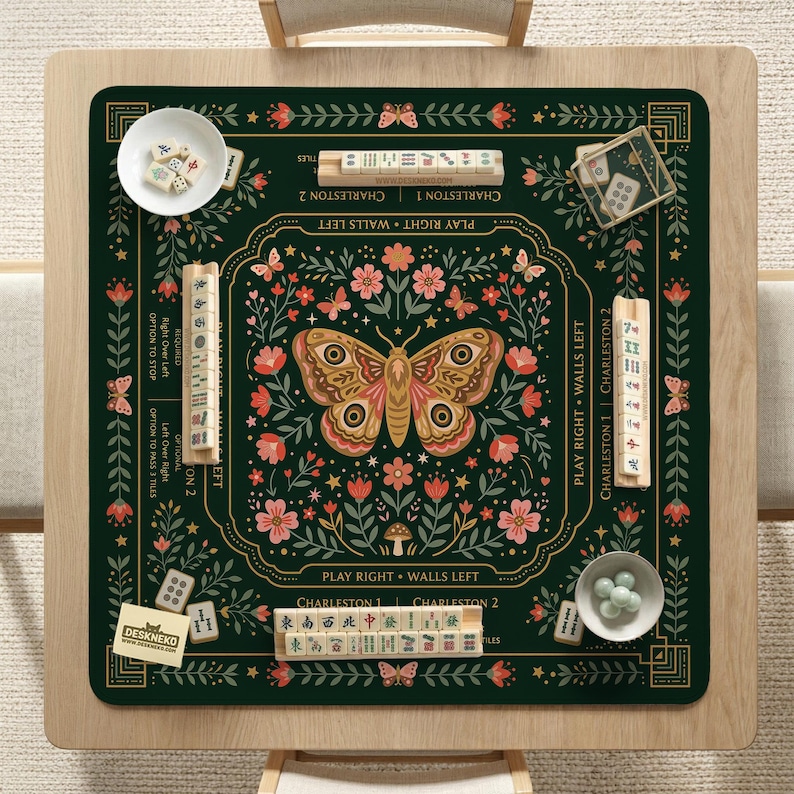 May include: A dark green square mahjong mat featuring a central moth illustration surrounded by floral patterns. The mat includes printed text such as Charleston 1, Charleston 2, Play Right, and Walls Left, with four wooden tile racks and game tiles.