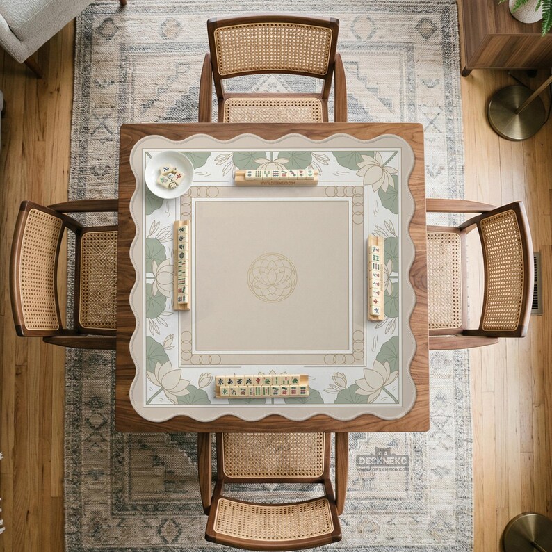 May include: Overhead view of a square wooden Mahjong table with four matching chairs. The table has a beige playing surface with a floral border and a lotus flower design. The chairs have woven cane backs and seats.