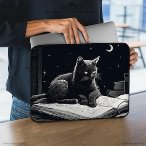 May include: Laptop sleeve with a black cat design, set against a night sky with stars and a crescent moon. The cat is lying on an open book. The sleeve has the text "DESKNEKO" and website addresses. The design is in black and white.