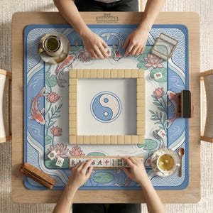 May include: A wooden mahjong table with a blue and white mat featuring koi carp, lotus flowers, and a yin-yang symbol. The table is set for a game, with tiles and tea cups visible. The brand name "DESKNEKO" is printed on the table.