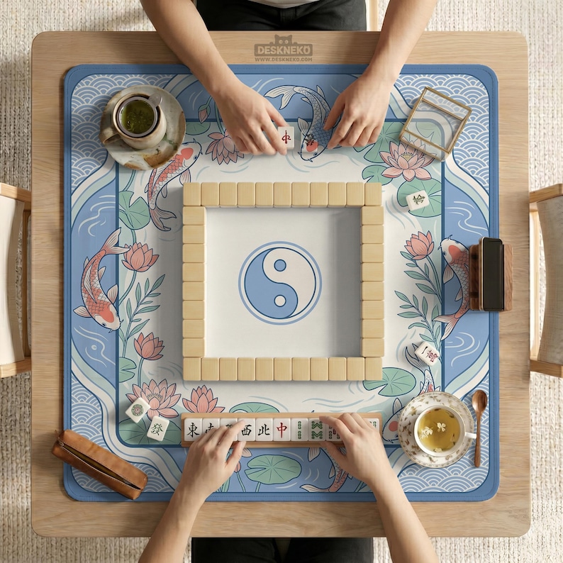 May include: A wooden mahjong table with a blue and white mat featuring koi carp, lotus flowers, and a yin-yang symbol. The table is set for a game, with tiles and tea cups visible. The brand name "DESKNEKO" is printed on the table.