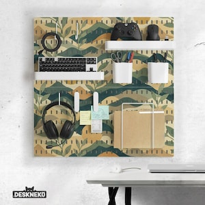 Pode incluir: Um painel perfurado com um padrão de paisagem verde, amarelo e castanho, contendo um teclado, auscultadores e outros materiais de escritório. Inclui uma prateleira branca com um comando de jogo preto e um rato. O painel tem uma moldura branca.