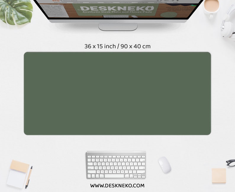 May include: A solid olive green desk mat, 36 x 15 inches, sits on a white desk. A computer monitor, keyboard, mouse, and other office supplies are arranged around the mat. The website address www.deskneko.com is visible.