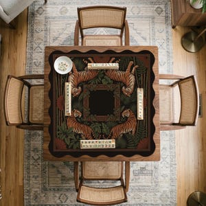 May include: A square wooden mahjong table with a decorative playing surface featuring tigers and foliage. The table is surrounded by four cane-backed chairs. A small white bowl and mahjong tiles are on the table.