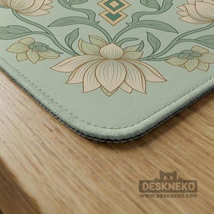 May include: A rectangular desk mat featuring a light sage green background with a repeating floral pattern of cream-colored lotus flowers and dark green stems. The mat has stitched edges and includes the text DESKNEKO and WWW.DESKNEKO.COM.