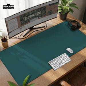 May include: A teal desk mat with a computer monitor, keyboard, mouse, and headphones on a wooden desk. The monitor displays the website "DESKNEKO". A small plant and a pencil holder are also visible.