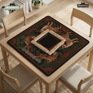 May include: A square desk mat featuring a tiger and foliage design in shades of orange, brown, and green. The mat has a black center and a wooden frame. The mat is on a wooden table with chairs.