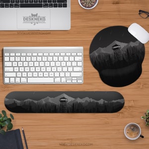 May include: A computer desk setup featuring a keyboard, mouse, and mousepad with a mountain and forest design. The wrist rest and mousepad have a black and gray landscape illustration. The text "DESKNEKO" and "WWW.DESKNEKO.COM" are visible.