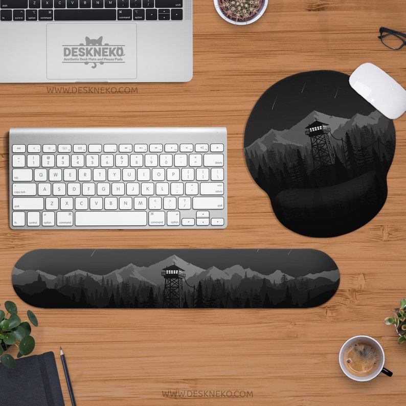 May include: A computer desk setup featuring a keyboard, mouse, and mousepad with a mountain and forest design. The wrist rest and mousepad have a black and gray landscape illustration. The text "DESKNEKO" and "WWW.DESKNEKO.COM" are visible.