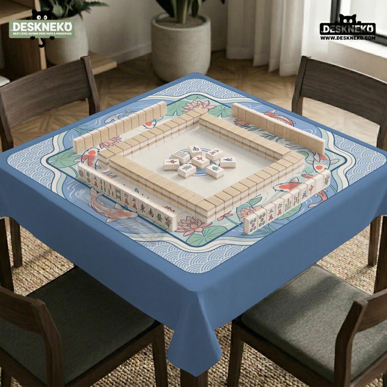 May include: A blue square tablecloth with a decorative border featuring koi carp and lotus flowers. A Mahjong set is arranged on the table, with wooden tiles and racks. The image includes the text "DESKNEKO".